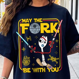 May include: Navy blue t-shirt with a yellow and red graphic featuring a cartoon fork character with lightsabers and the text "MAY THE FORK BE WITH YOU". The design includes a Death Star, spaceships, and stars.