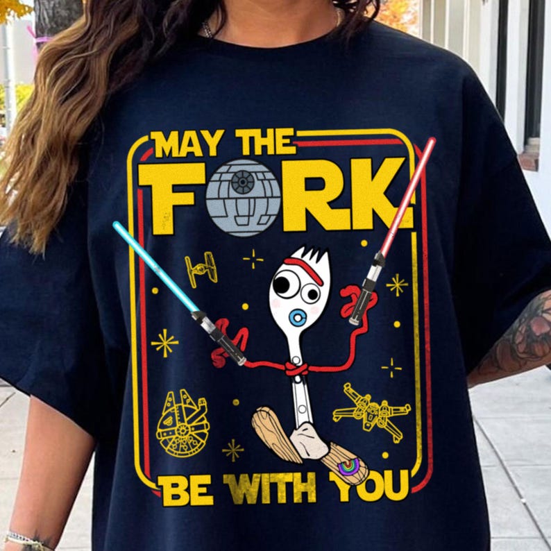 May include: Navy blue t-shirt with a yellow and red graphic featuring a cartoon fork character with lightsabers and the text "MAY THE FORK BE WITH YOU". The design includes a Death Star, spaceships, and stars.