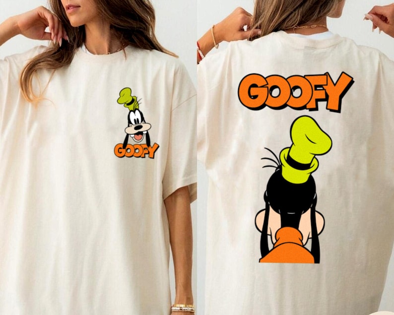 Puede incluir: Camiseta color crema con una imagen de dibujos animados de Goofy en la parte delantera y trasera. La parte delantera muestra la cara de Goofy y la palabra "GOOFY" en naranja. La parte trasera muestra la cabeza de Goofy y la palabra "GOOFY" en naranja.