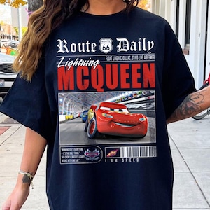 Op de afbeelding: Zwart T-shirt met een afbeelding van Lightning McQueen uit de film Cars. De afbeelding bevat de tekst "Route 66 Daily", "Lightning McQueen", "Float like a Cadillac, Sting like a Beemer" en "I am Speed".
