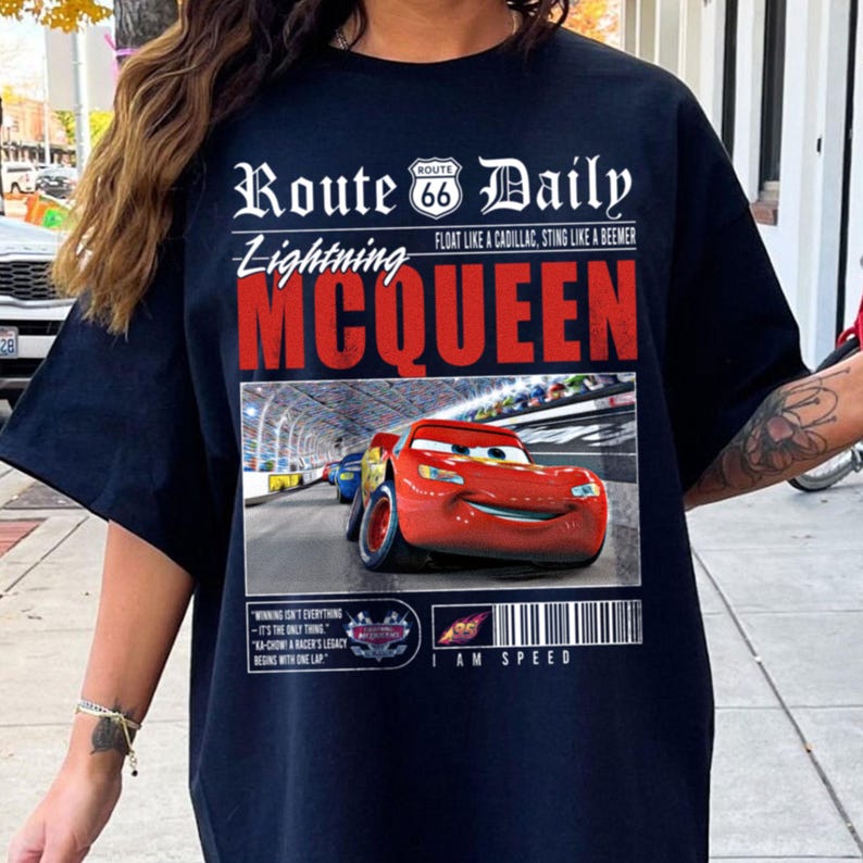 Op de afbeelding: Zwart T-shirt met een afbeelding van Lightning McQueen uit de film Cars. De afbeelding bevat de tekst "Route 66 Daily", "Lightning McQueen", "Float like a Cadillac, Sting like a Beemer" en "I am Speed".