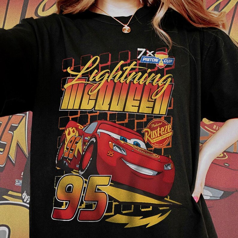May include: Black t-shirt featuring a graphic of Lightning McQueen, a red race car with the number 95. The design includes the text "Lightning McQueen" in yellow and red, along with "7x Piston Cup" and "Rusteze" logos.