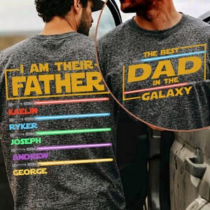 May include: Grey t-shirt featuring the phrases "I AM THEIR FATHER" and "THE BEST DAD IN THE GALAXY" in yellow. The names Kaelin, Ryker, Joseph, Andrew, and George are below, each with a coloured lightsaber design.