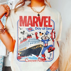 May include: Cream-colored t-shirt featuring a Marvel Day at Sea design. The graphic includes the word "MARVEL" in red, a cruise ship, and a cartoon character dressed as Captain America. The shirt also has the text "Custom-Name".