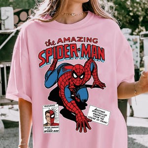 Może przedstawiać: Jasnor&oacute;żowa koszulka z komiksową grafiką Spider-Mana. Projekt przedstawia Spider-Mana w akcji, z napisem "the AMAZING SPIDER-MAN". Zawiera panel z Peterem Parkerem. Swobodny top dla fan&oacute;w serii komiks&oacute;w.