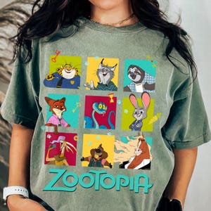 Puede incluir: Camiseta verde salvia con una cuadr&iacute;cula de personajes de Zootopia en cuadrados coloridos. El logotipo turquesa de Zootopia est&aacute; impreso debajo. La camiseta tiene un corte holgado y mangas cortas.