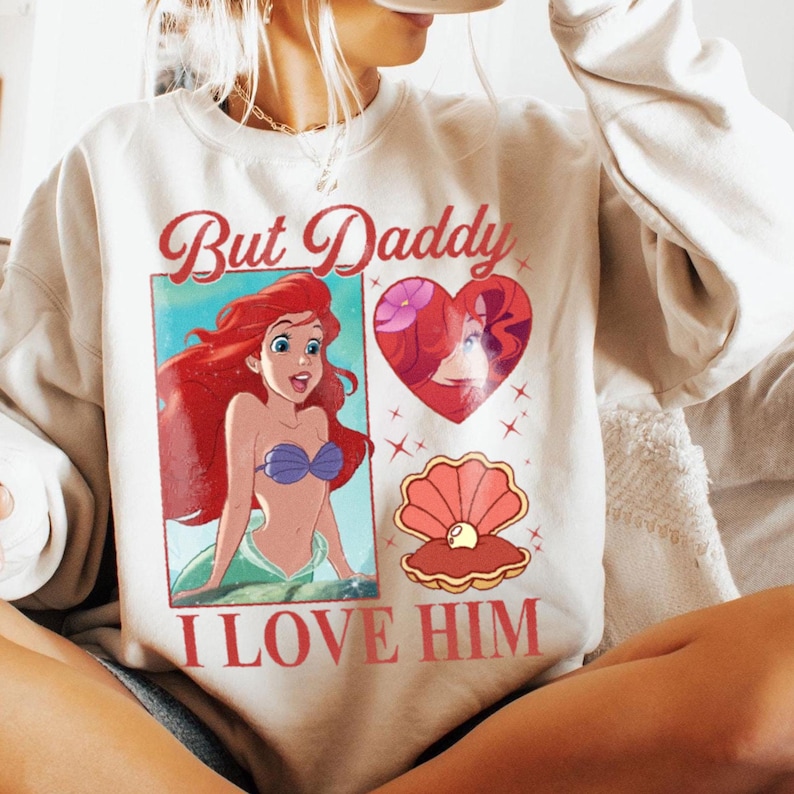 May include: A white sweatshirt with a graphic print of Ariel from The Little Mermaid. The text on the sweatshirt reads "But Daddy I Love Him".