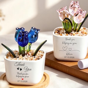 May include: Two white square ceramic planters containing glass tulips. One planter features blue glass tulips with text reading Thank You, Thank you for helping me grow, and 07.13.2026. The other has pink glass tulips with Thank you helping me grow, Olivia, and 07.13.2026.