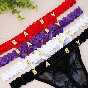 May include: Four pairs of black, white, purple, and red lace underwear with gold 'BABY' lettering on the waistband.