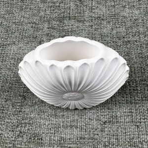 May include: A white, oval-shaped ceramic planter with a fluted, petal-like design. The interior is smooth and unadorned, contrasting with the textured exterior. The planter is suitable for small plants or decorative use.