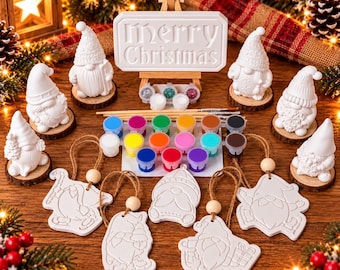 May include: A DIY Christmas painting kit featuring four white ceramic gnome figurines on wood slices, five hanging gnome ornaments with twine, and a central sign reading Merry Christmas on a wooden easel, plus paint pots and brushes.