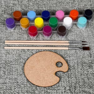 May include: A craft kit with a wooden palette, three paintbrushes, and a set of 12 colorful paint pots. The paint colors include purple, orange, blue, yellow, pink, green, white, and brown.