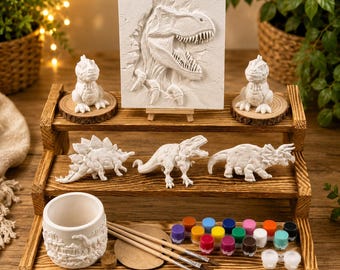 May include: A wooden tiered display holds a collection of dinosaur-themed craft supplies. Includes a T-Rex relief, dinosaur figurines, a paintable cup, paint pots, and paintbrushes. The display is made of light brown wood.