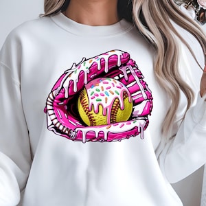 Puede incluir: Sudadera blanca con un gr&aacute;fico rosa y amarillo de una pelota de softbol en un guante de receptor con glaseado rosa y chispas.