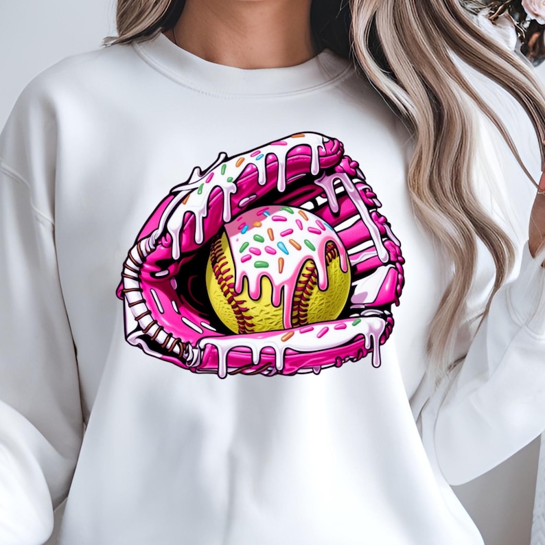 Puede incluir: Sudadera blanca con un gr&aacute;fico rosa y amarillo de una pelota de softbol en un guante de receptor con glaseado rosa y chispas.