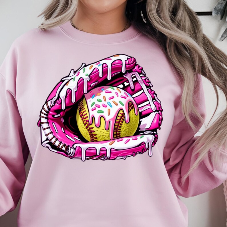 Puede incluir: Sudadera rosa con un gr&aacute;fico de un guante de softbol rosa y blanco con una pelota de softbol amarilla cubierta de glaseado blanco y chispas de colores.
