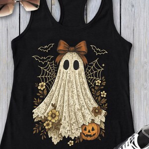 K&ouml;nnte beinhalten: Schwarzes Tanktop mit einem Halloween-Geister-Design. Der Geist ist in ein wei&szlig;es Spitzentuch mit einer braunen Schleife geh&uuml;llt, umgeben von Spinnweben, Flederm&auml;usen, Blumen und einem K&uuml;rbis.