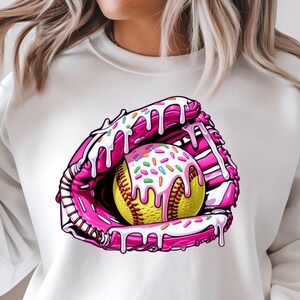 Puede incluir: Una sudadera blanca con un gr&aacute;fico rosa y blanco de una pelota de softball en un guante rosa y blanco con glaseado blanco y chispas.