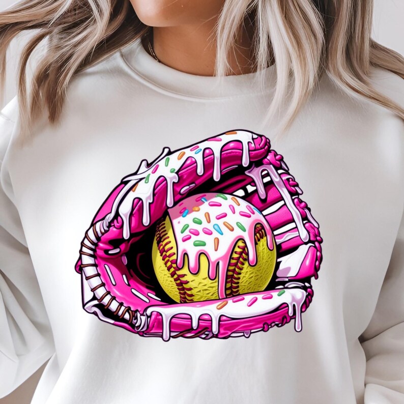 Puede incluir: Una sudadera blanca con un gr&aacute;fico rosa y blanco de una pelota de softball en un guante rosa y blanco con glaseado blanco y chispas.