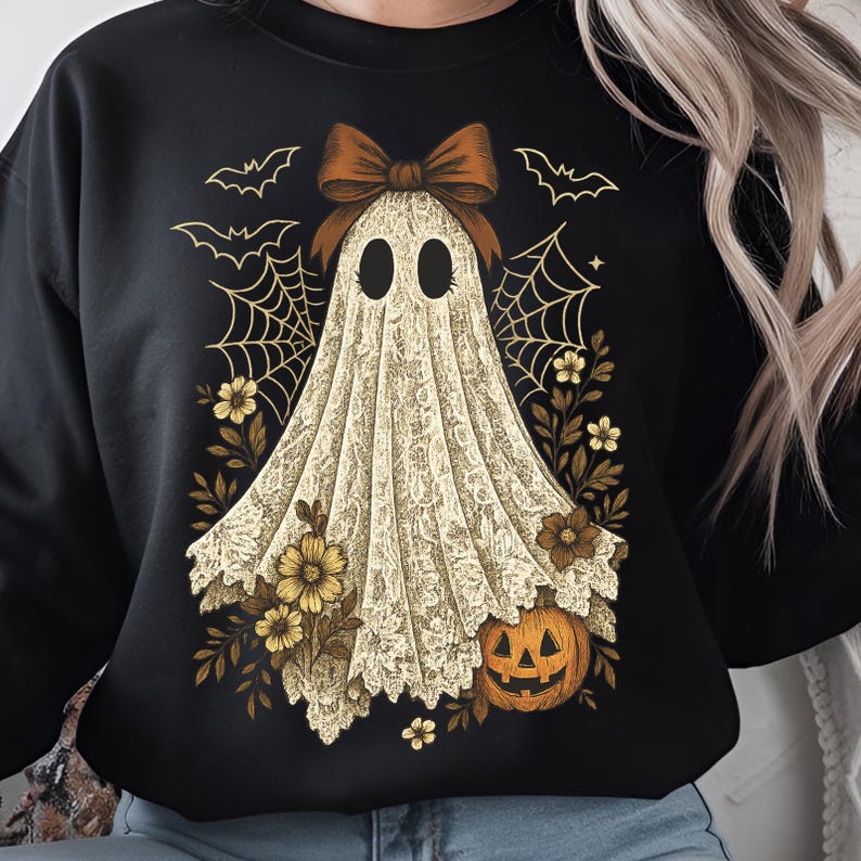 K&ouml;nnte beinhalten: Schwarzes Sweatshirt mit einem Geisterdesign, das eine Schleife, Spinnweben, Blumen, Flederm&auml;use und einen K&uuml;rbis zeigt. Der Geist ist in einem spitzenartigen Stoff drapiert. Ein Halloween-Motiv.