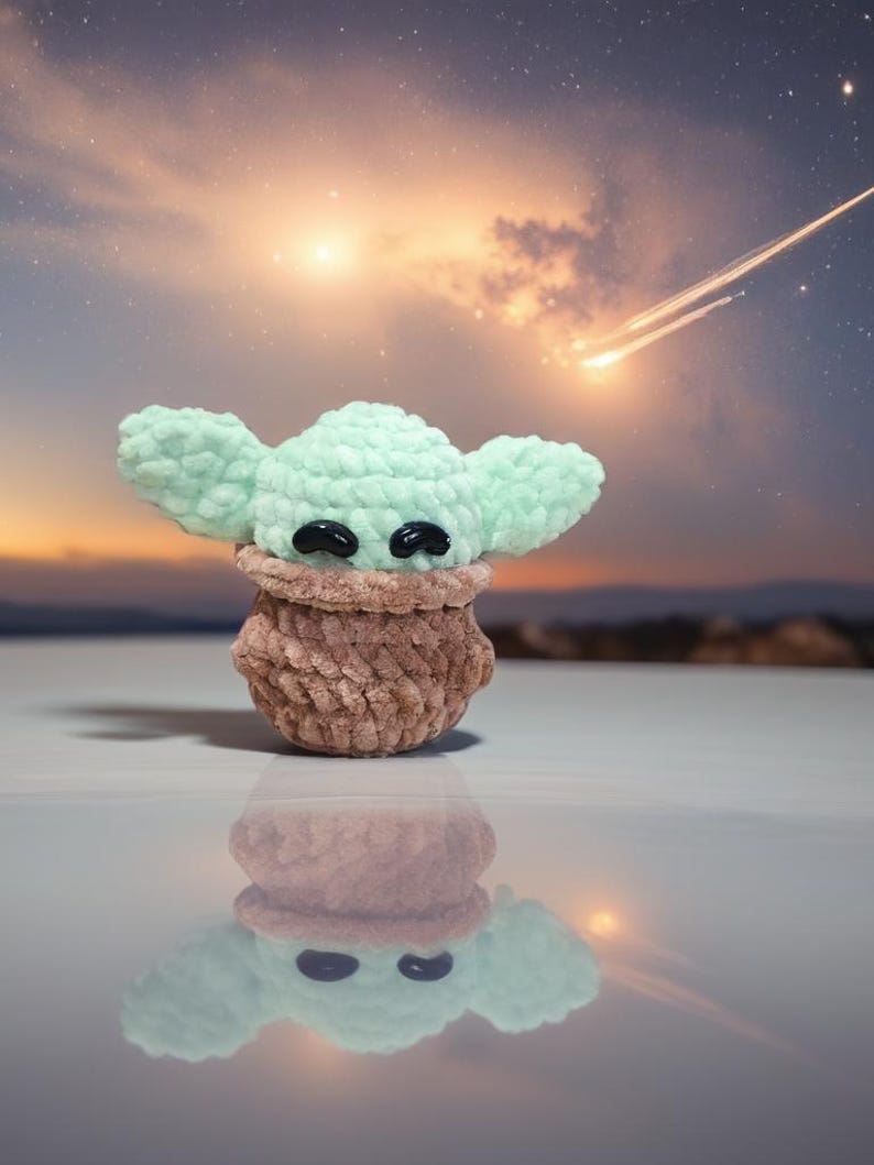 May include: A handmade crochet figure of a character with large ears and black eyes. The figure is light green with a brown base. The background features a sunset with a starry sky and a shooting star.