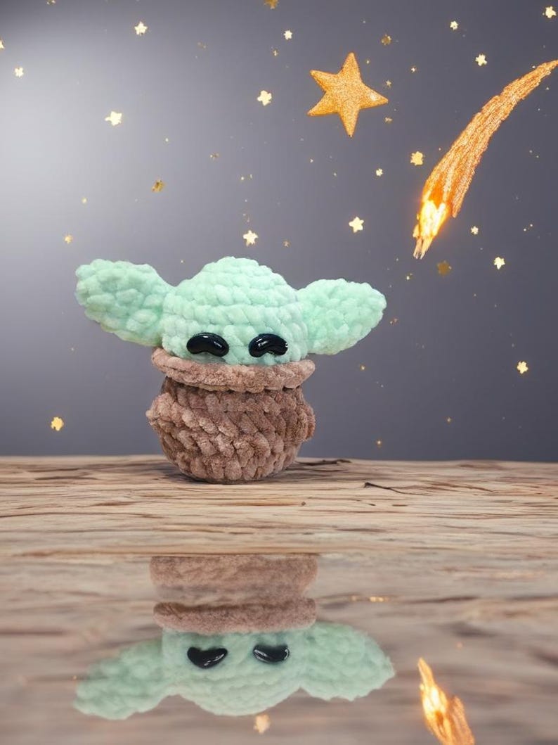 May include: A handmade crochet figure of a character with large ears, in mint green and brown. The figure has black eyes and is set against a starry background with a shooting star. The figure is reflected in a glossy surface.