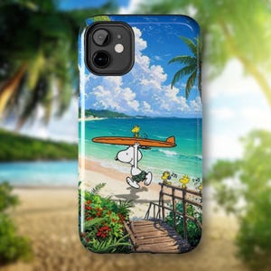 Puede incluir: Funda de teléfono con una vibrante escena de playa, con Snoopy llevando una tabla de surf. El diseño muestra un cielo azul, agua turquesa y una playa de arena. Palmeras y personajes de dibujos animados completan el tema tropical.