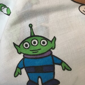 Op de afbeelding: Een groene alien met drie ogen en een paarse kraag draagt een blauw pak. De alien staat op een witte achtergrond.