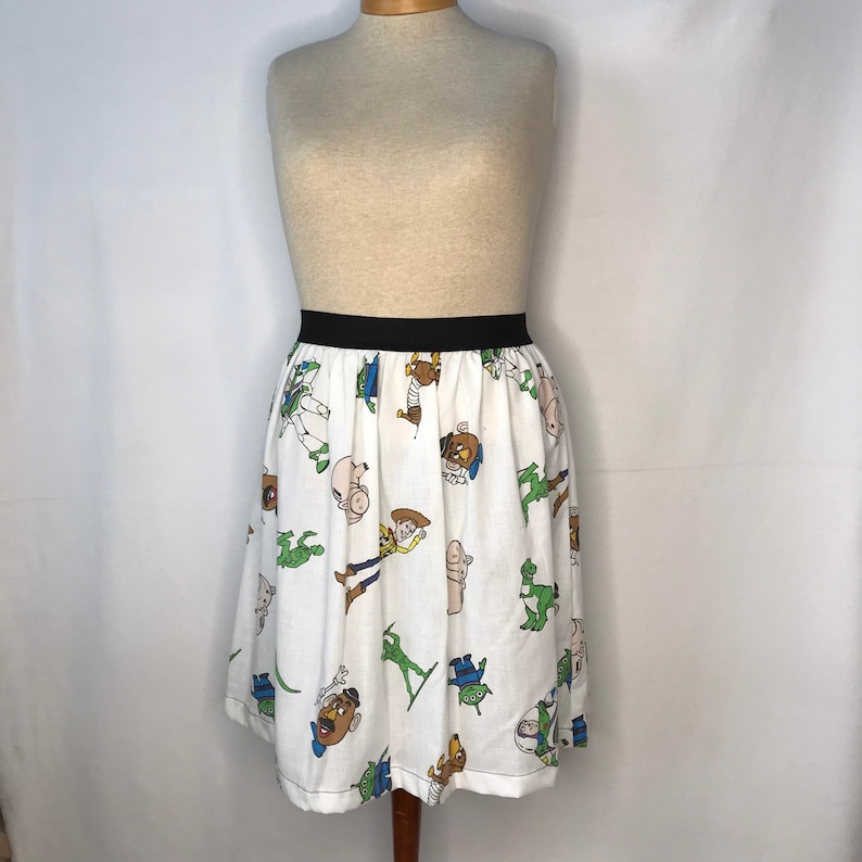 Op de afbeelding: Een witte rok met een zwarte tailleband en een patroon van Toy Story-personages, waaronder Woody, Buzz Lightyear en Mr. Potato Head.