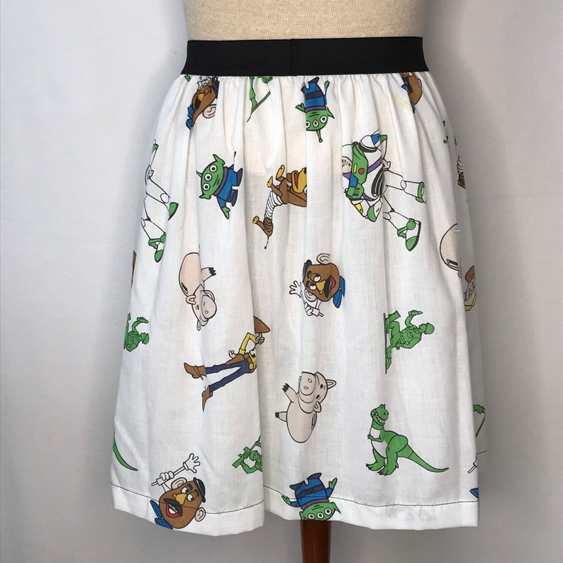 Op de afbeelding: Een witte rok met een zwarte tailleband met een herhalend patroon van personages uit de Toy Story-franchise. De personages zijn Woody, Buzz Lightyear, Rex en Mr. Potato Head.