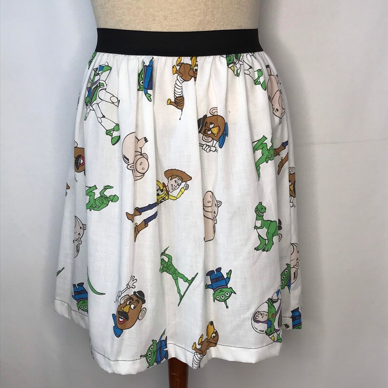 Op de afbeelding: Een witte rok met een zwarte tailleband met een herhalend patroon van Toy Story-personages, waaronder Woody, Buzz Lightyear en de aliens.