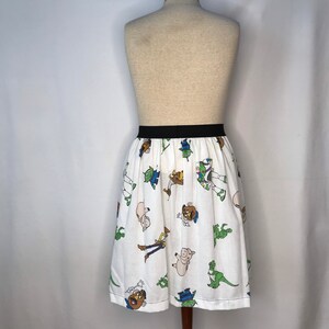 Op de afbeelding: Een witte rok met een zwarte tailleband en een patroon van Toy Story-personages. De personages zijn Woody, Buzz Lightyear, Rex en Mr. Potato Head.