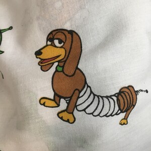 Op de afbeelding: Een cartoonillustratie van een bruine en gele hond met een wit verband om zijn lichaam. De hond heeft een veerachtige staart en kijkt naar links.