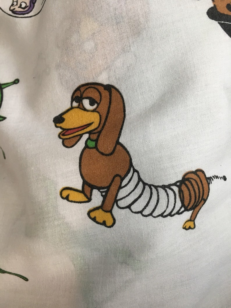 Op de afbeelding: Een cartoonillustratie van een bruine en gele hond met een wit verband om zijn lichaam. De hond heeft een veerachtige staart en kijkt naar links.