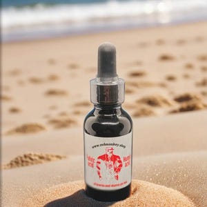 Peut inclure: Une bouteille en verre foncé avec un compte-gouttes et une étiquette rouge et blanche. L'étiquette représente un homme de dessin animé portant une veste rouge et un chapeau noir. Le texte sur l'étiquette indique "www.redmonkey.shop" et "Acide Hyaluronique". La bouteille est posée sur une plage de sable.