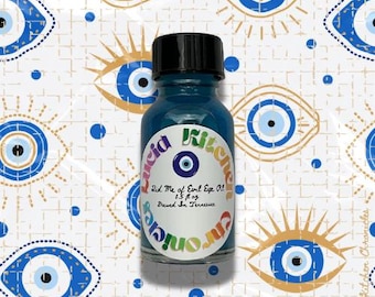 May include: A small, teal-colored glass bottle with a black cap. The bottle has a label with the text "Lucid Kitchen Chronicles" and "Did Me of Evil Eye Oil". The background features a repeating pattern of blue and gold evil eye designs.