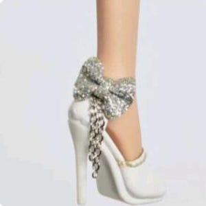 May include: White high-heeled shoe with a silver glitter bow and dangling chain detail. The shoe has a pointed toe and a stiletto heel. The bow is large and prominent, adding a touch of glamour to the design.