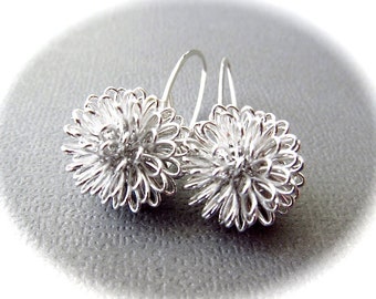 May include: A pair of silver earrings with a delicate, flower-like design. Each earring is made of a cluster of small, interconnected loops of wire, creating a three-dimensional, airy effect.