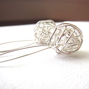 May include: A pair of silver dangle earrings with a wire-wrapped sphere design. The spheres are made of thin wire that is woven together to create a delicate, openwork pattern.