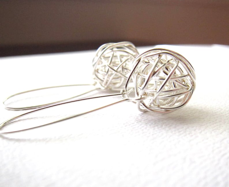 May include: A pair of silver dangle earrings with a wire-wrapped sphere design. The spheres are made of thin wire that is woven together to create a delicate, openwork pattern.