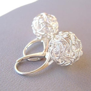 May include: Silver earrings featuring a delicate, intricate wire design resembling a cage or web. The earrings are crafted from a single piece of wire twisted and shaped into a sphere.