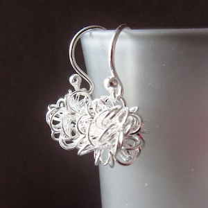 May include: Silver dangle earrings with a delicate, intricate design resembling a cluster of small, intertwined circles.