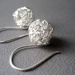 May include: A pair of silver earrings with a delicate, intricate wire design. Each earring features a spherical shape with a woven wire pattern, creating a unique and modern look.