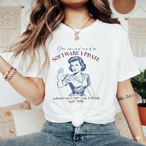 May include: White t-shirt with a retro-style illustration of a woman and the text "You remind me of a SOFTWARE UPDATE whenever I see you I think 'NOT NOW'". The design is in shades of blue and maroon.