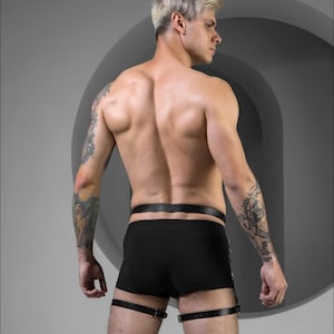 May include: A person wearing black underwear and leather leg straps. The straps have buckles and are adjustable.