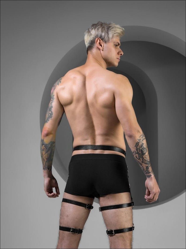 May include: A person wearing black underwear and leather leg straps. The straps have buckles and are adjustable.
