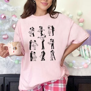 Puede incluir: Una camiseta rosa con un gr&aacute;fico de nueve parejas bailando. Las parejas est&aacute;n todas en silueta y visten ropa sencilla. La camiseta es de corte holgado y tiene cuello redondo.