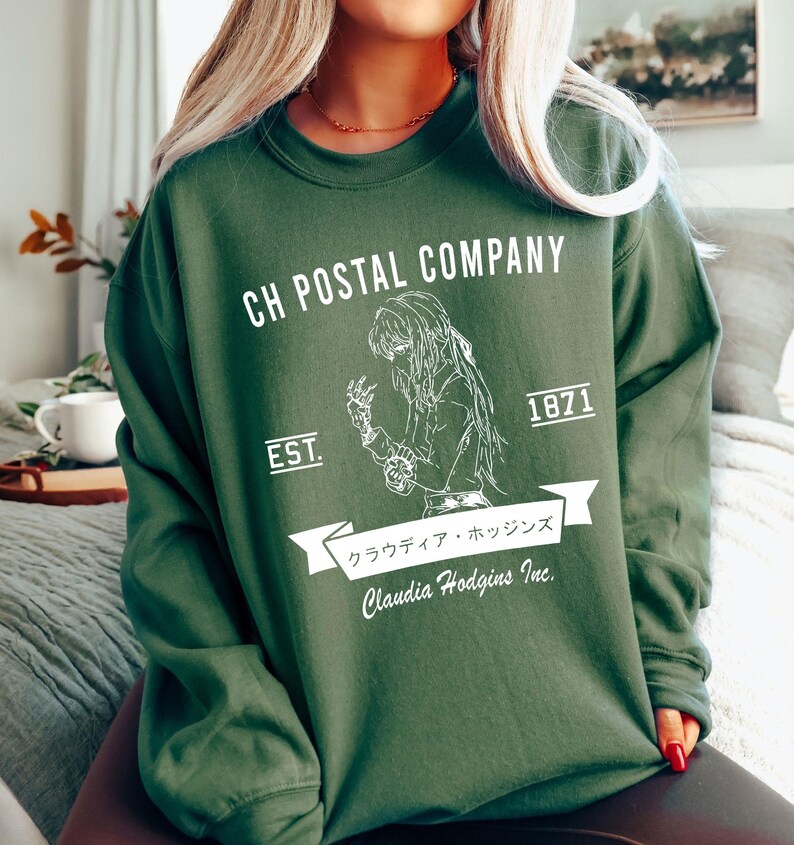 May include: Dark green sweatshirt with white graphic text and illustration. The text reads "CH POSTAL COMPANY" above an illustration of a person. Below the illustration is the text "Claudia Hodgins Inc." and Japanese text.