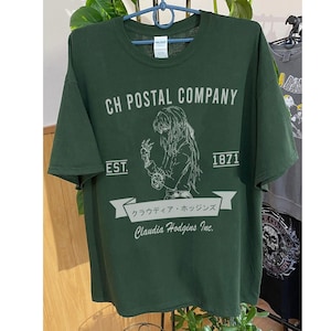 May include: Dark green t-shirt with the text "CH POSTAL COMPANY" and a graphic of a person. Below the graphic is the text "Claudia Hodgins Inc." and Japanese text. The shirt also has the text "EST. 1871".