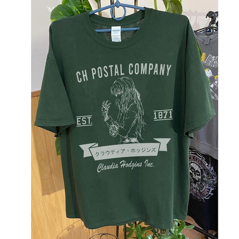 May include: Dark green t-shirt with the text "CH POSTAL COMPANY" and a graphic of a person. Below the graphic is the text "Claudia Hodgins Inc." and Japanese text. The shirt also has the text "EST. 1871".